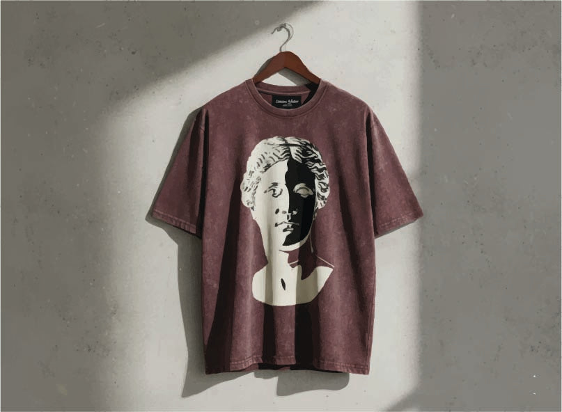 Maroon T -shirt with a graphic design of a face on a hanger against a gray wall.